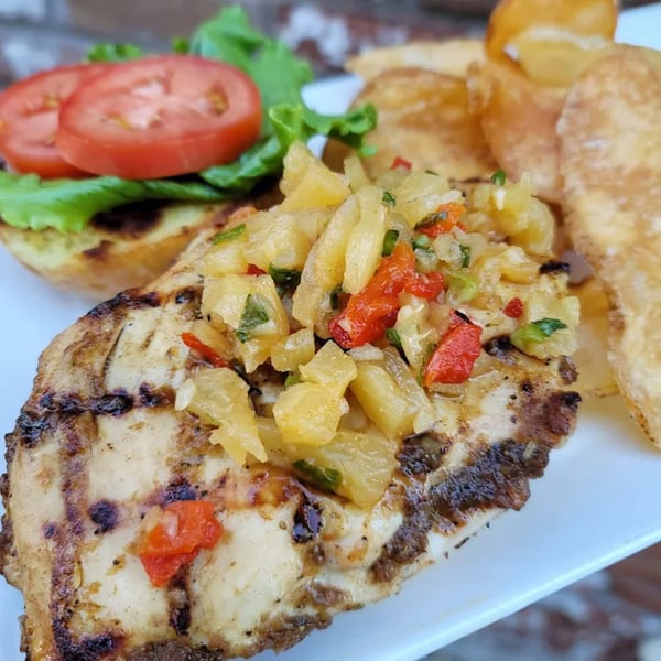Grilled chicken topped with pineapple salsa, served with a bun, lettuce, tomato, and potato chips.