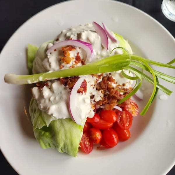 Wedge salad with blue cheese dressing, bacon, red onion, cherry tomatoes, and green onion.