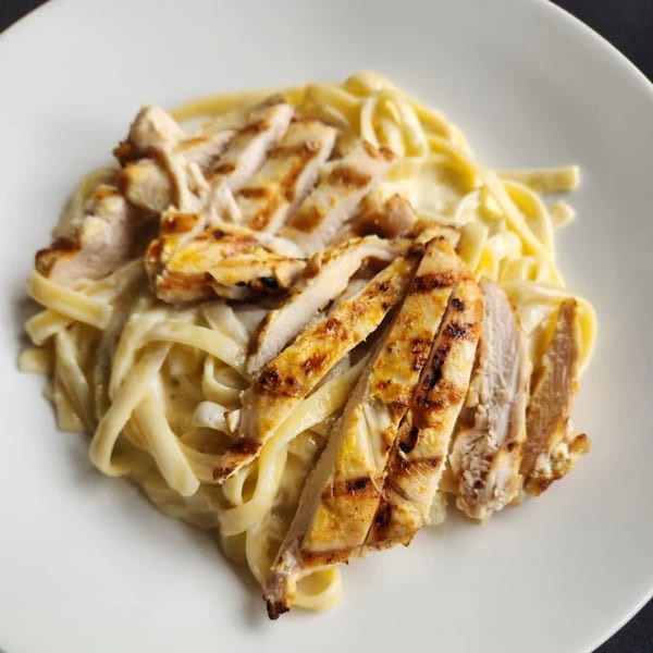 Grilled chicken fettuccine alfredo on a white plate, a classic American dish.