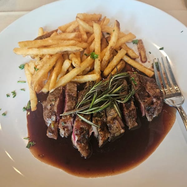 Sliced steak with rosemary and a side of french fries, served on a white plate with sauce.